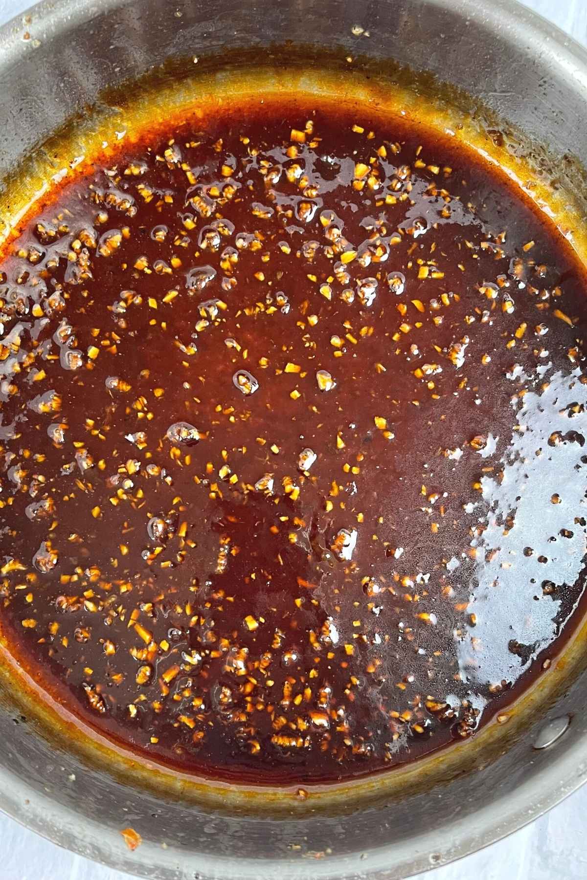 Thick glossy garlic sauce simmering in a pan with bits of minced garlic throughout.