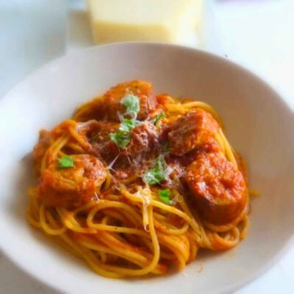 Bowl of spaghetti tossed with chicken sausage slices in marinara sacue, garnished with grated parmesan and fresh basil.