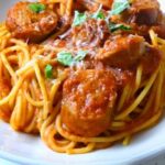 Close up view of chicken sausage spaghetti in a rich tomato sauce, sprinkled with shredded parmesan and fresh basil.