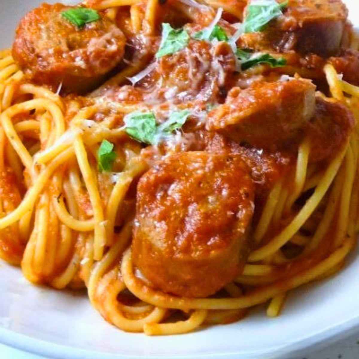 Close up view of chicken sausage spaghetti in a rich tomato sauce, sprinkled with shredded parmesan and fresh basil.