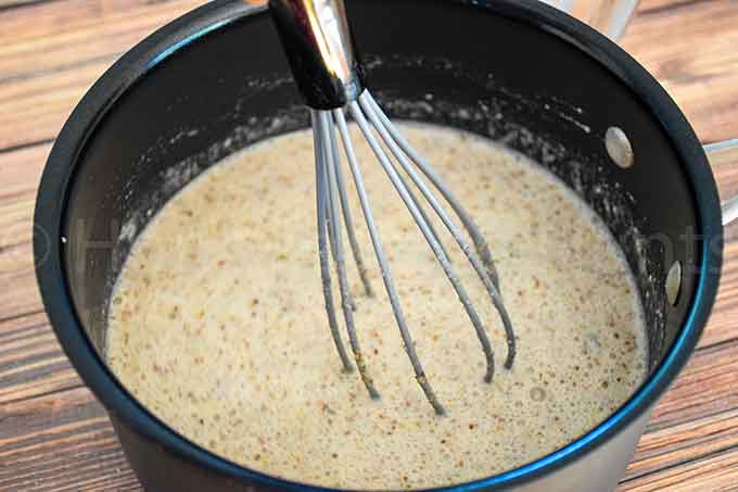 Chunky Monkey Noatmeal in a black saucepan being whisked, showing a thick speckled mixture as it heats.