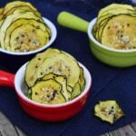 Thin dehydrated zucchini chips seasoned with everything bagel seasoning, served in colorful ramekins on a navy cloth.