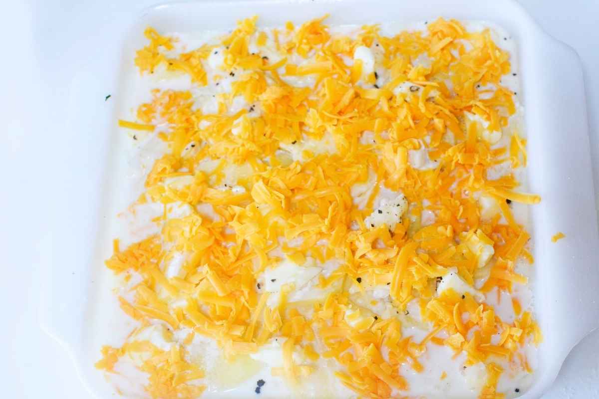 Unbaked scalloped potato casserole in a white dish, topped with shredded cheese and pepper over a creamy mixture.