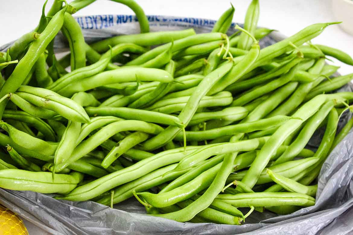 A pile of fresh green beans with stems, resting on a plastic bag on a countertop.