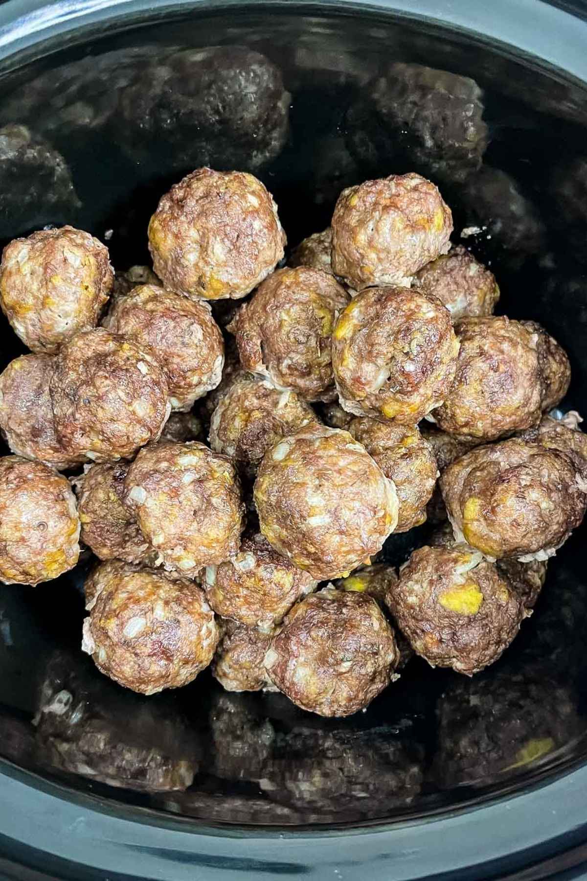 Meatballs piled in a black slow cooker, showing a browned cooked exterior.