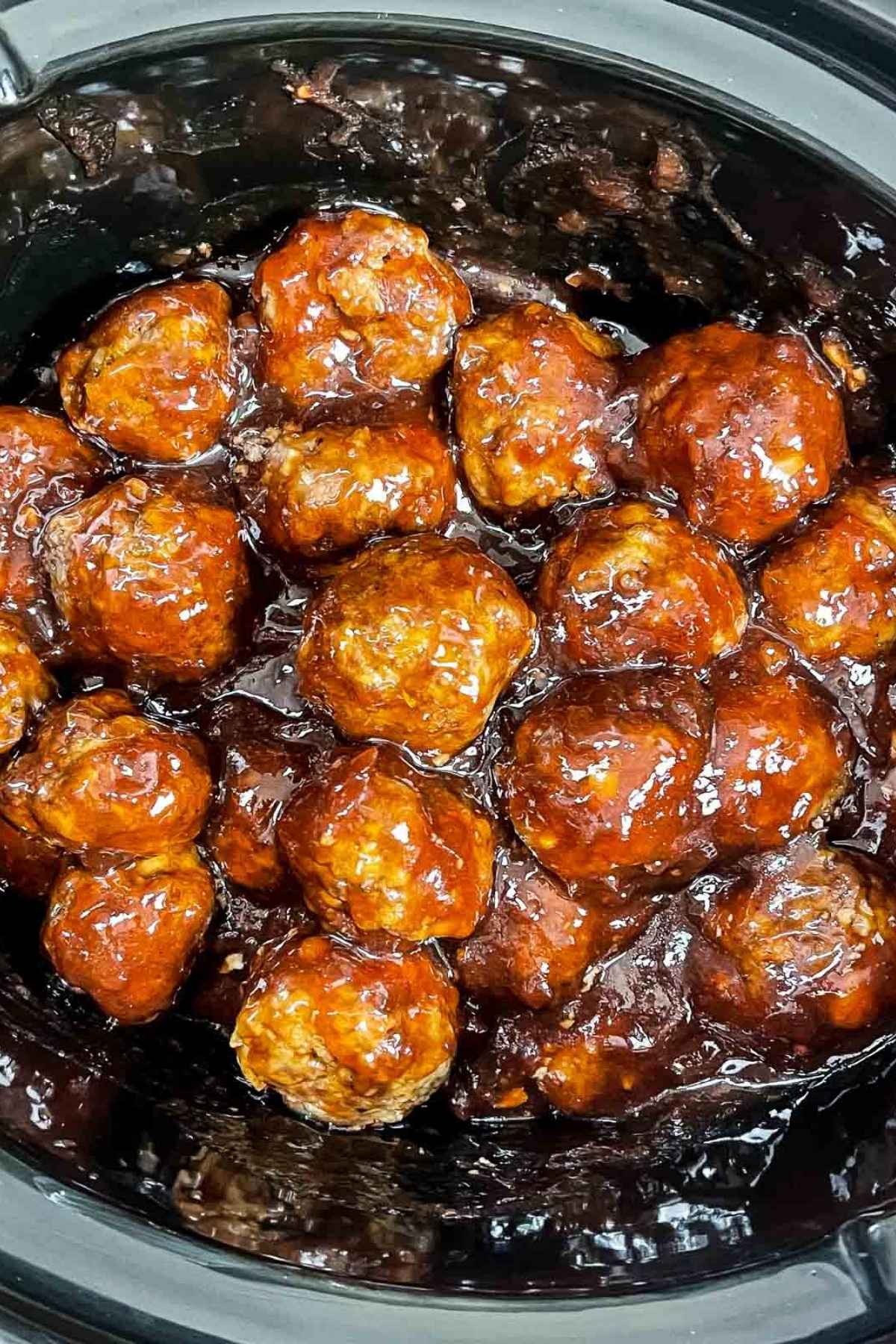 Cooked meatballs in a slow cooker coated in a thick, glossy BBQ and grape jelly sauce.