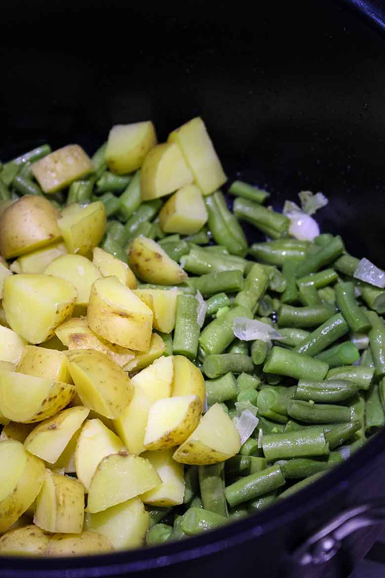 Chopped green beans, diced yellow potatoes, and shallots cooking in a black pot.