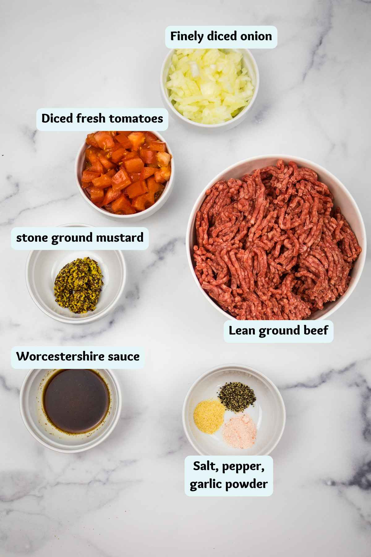 Labeled ingredients for ground beef sliders on a white marble background, featuring lean ground beef, diced onions, diced tomatoes, Worcestershire sauce, stone ground mustard, and a spice mix of salt, pepper, and garlic powder.