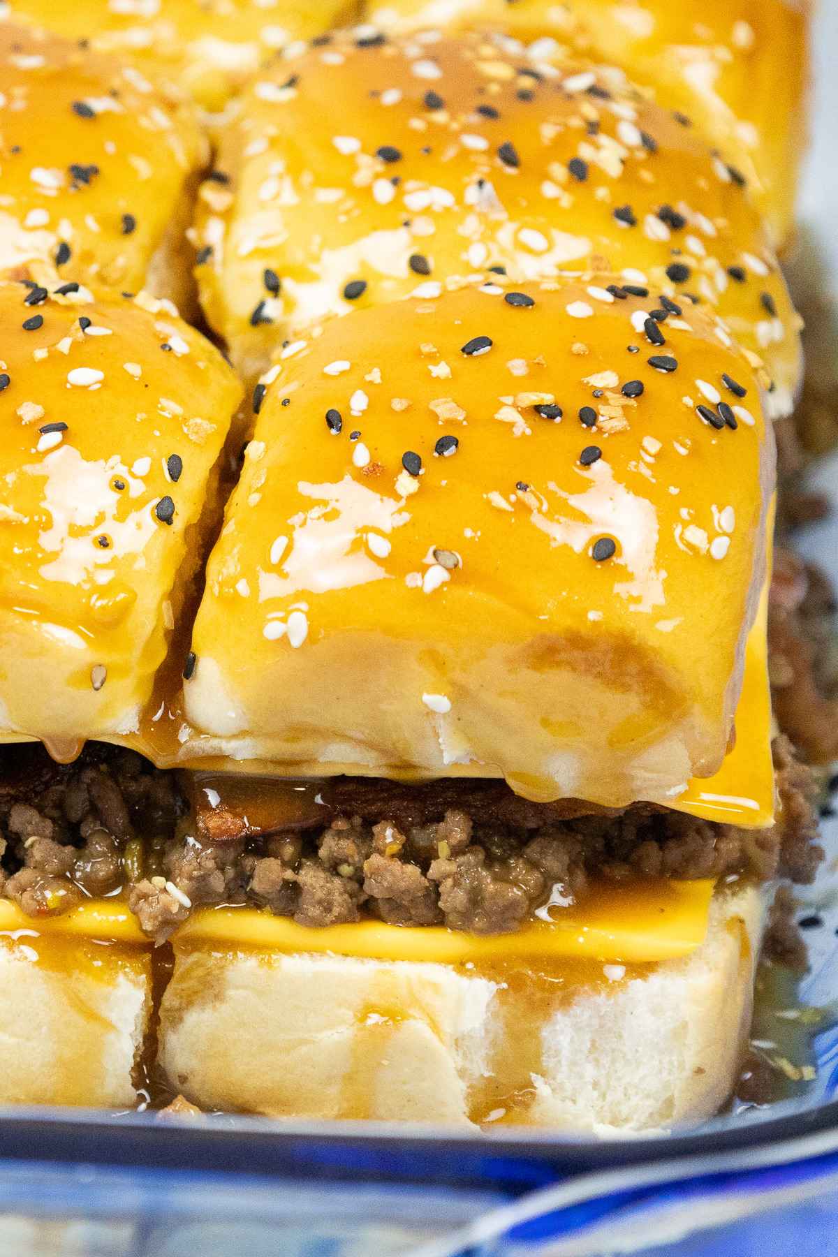 Close up of assembled ground beef slicers with golden buns, American cheese and bagel seasoning on top.