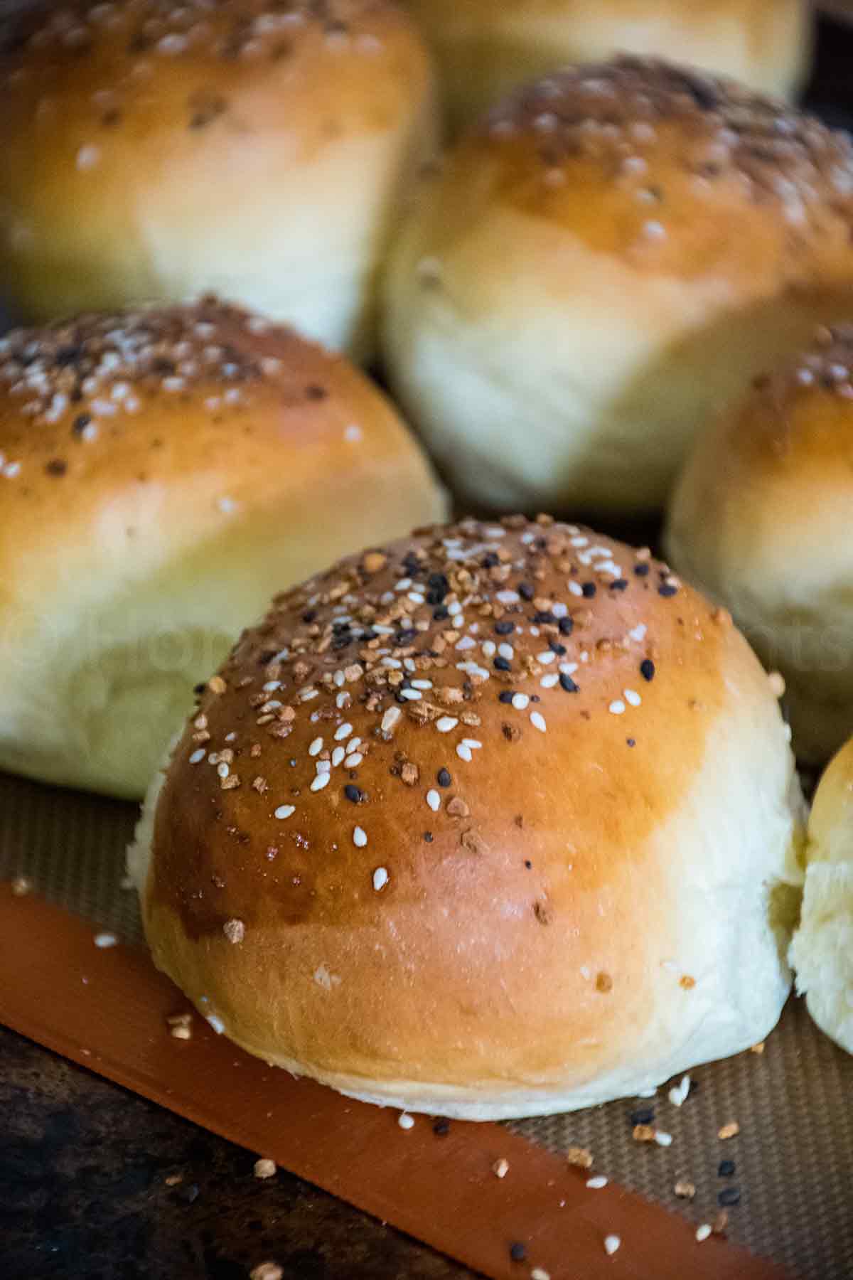 Close up of homemade hamburger buns topped with everything bagel seasoning, baked to a golden brown on a silicone mat.