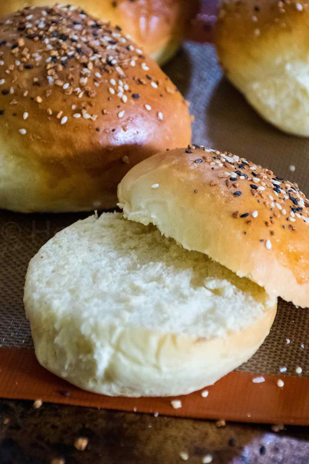 Burger roll sliced open to show soft fluffy interior with a golden brown, seeded top.