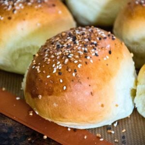 Close up of homemade hamburger buns topped with everything bagel seasoning, baked to a golden brown on a silicone mat.