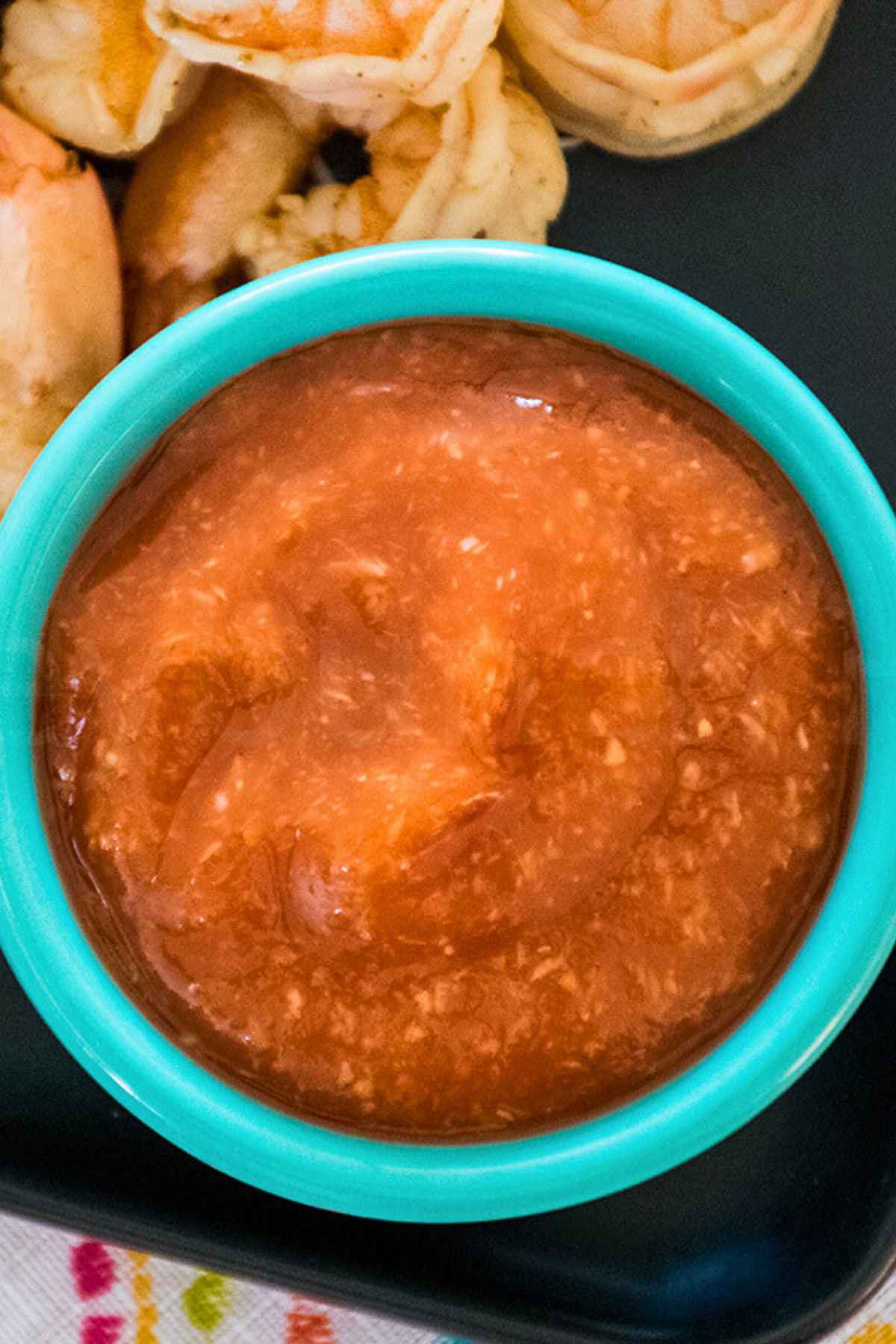 Overhead view of homemade cocktail sauce in a teal bowl next to a pile of shrimp, highlighting the sauce's slightly chunky texture.