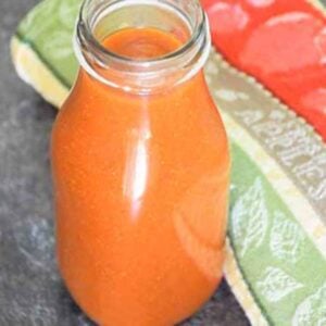 Pouring sauce into a glass bottle on a dark countertop, with orange-red sauce partway filled.