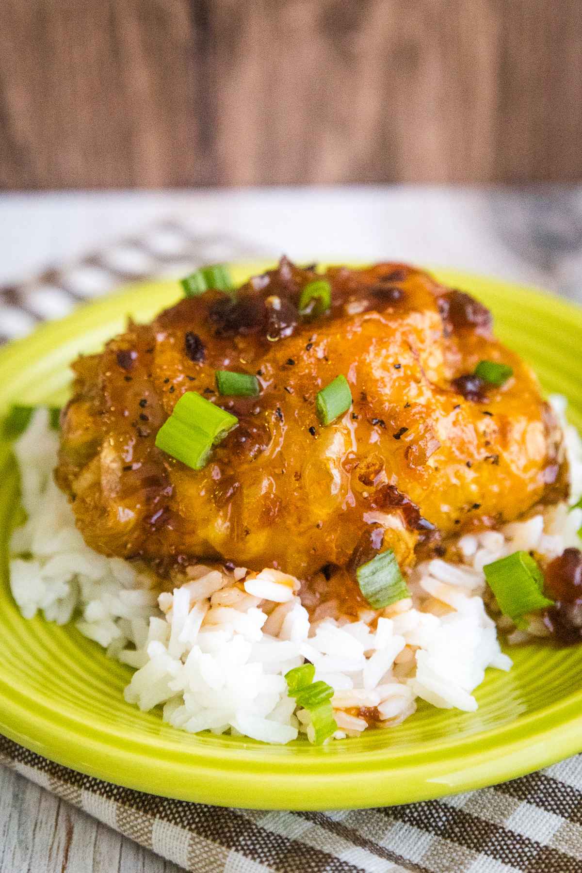 A glazed honey chipotle chicken thigh served over white rice on a bright green plate, garnished with chopped green onions.