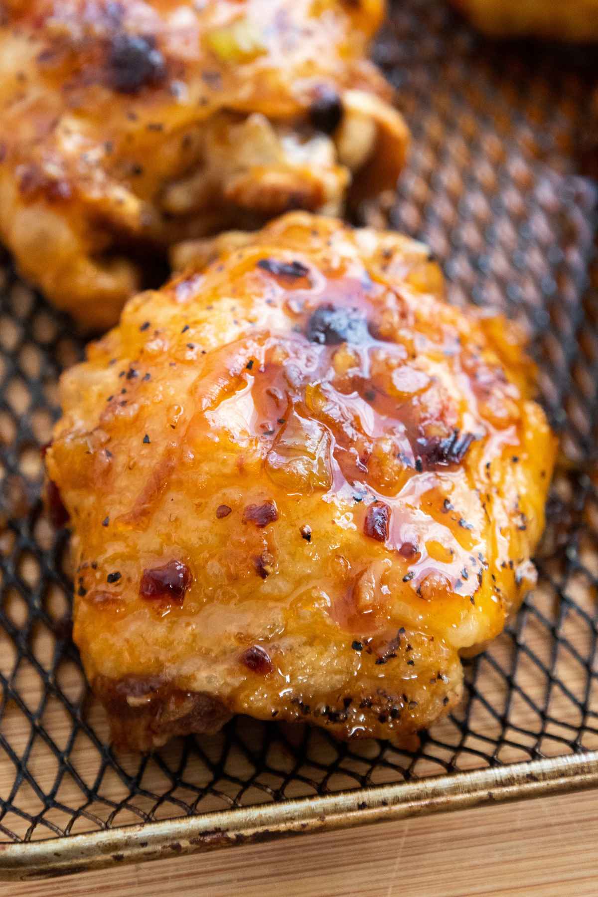 Crispy baked honey chipotle chicken thighs resting on an air fryer basket tray, with a caramelized glaze and black pepper flakes.