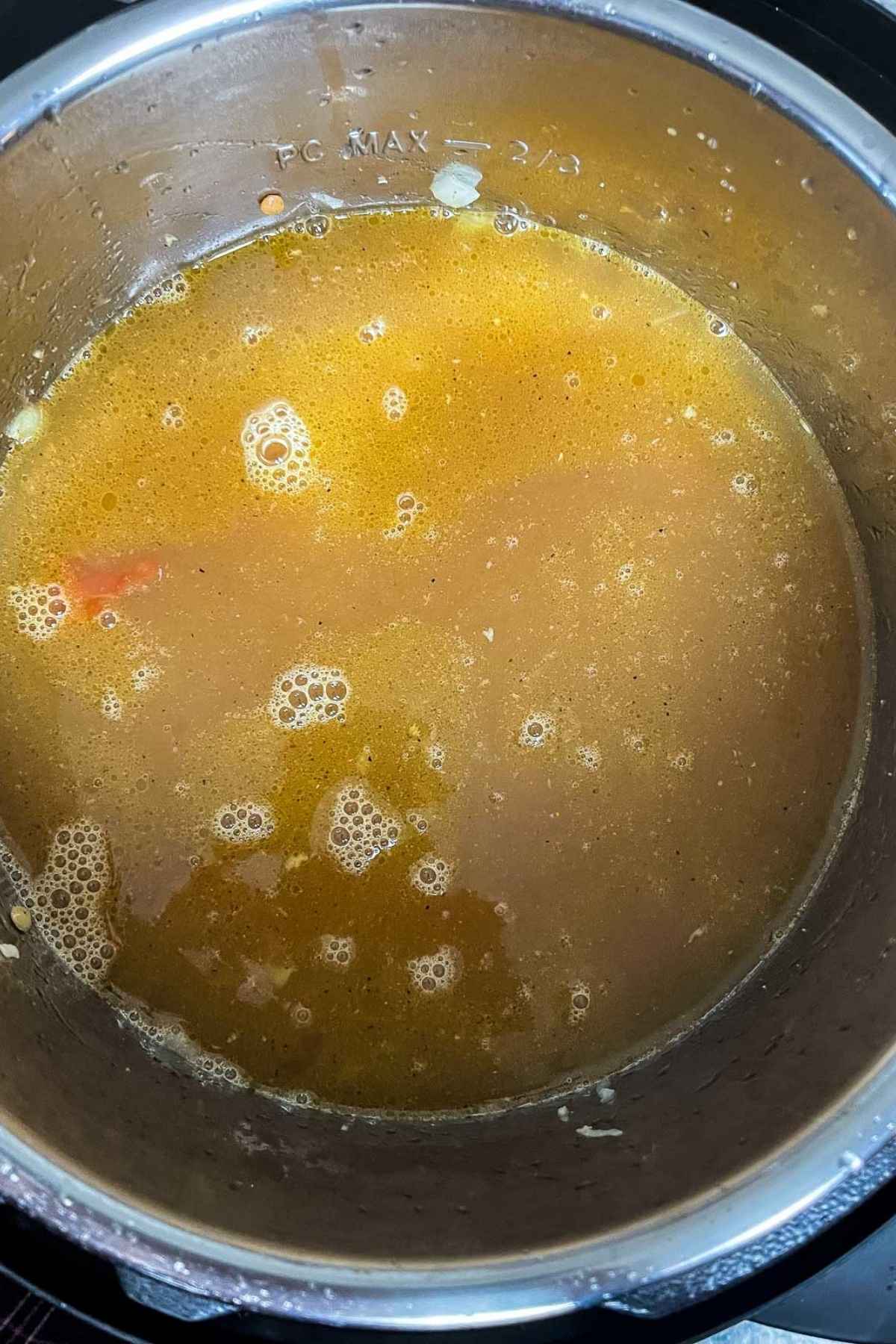 Close up of turkey lentil soup simmering in an Instant Pot, showing a golden broth with bits of onion and floating bubbles.