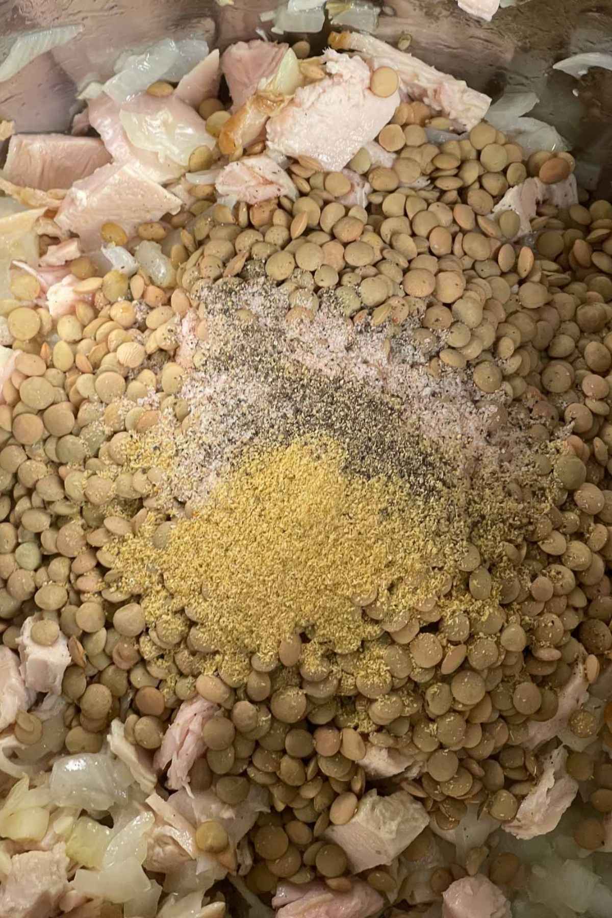 Close up of turkey lentil soup ingredients inside a pot, featuring uncooked lentils, diced onions, chopped turkey, and a colorful blend of seasonings.