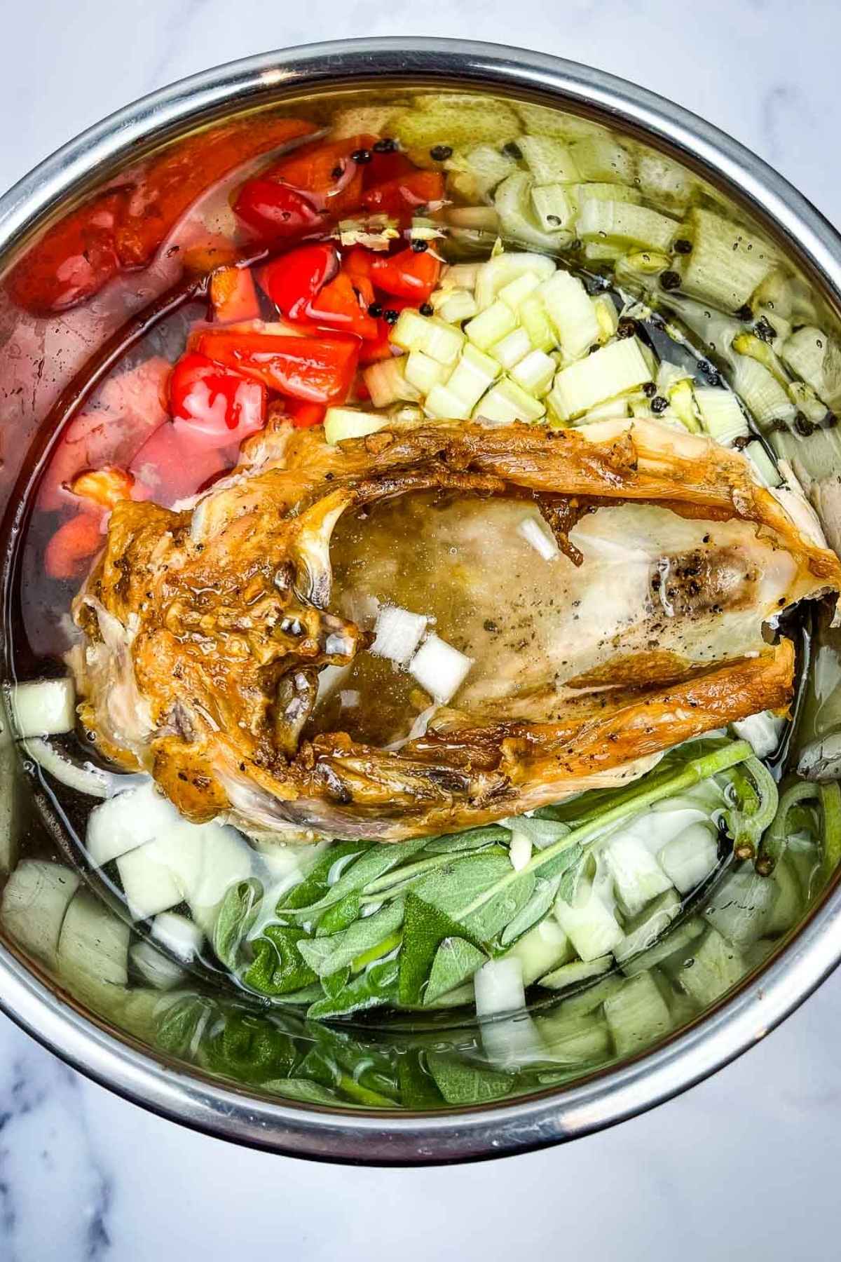 Instant pot filled with water, turkey carcass, chopped onions, celery, red bell peppers, sge, and whole peppercorns, ready to make a stock.