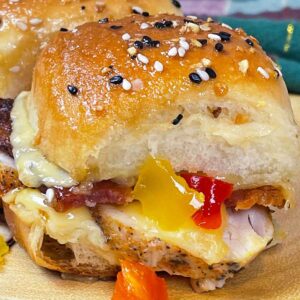 Close up of kentucky hot brown sliders with gooey melted cheese, sliced turky and peppers between toasted slider buns, topped with everything bagel seasoning.