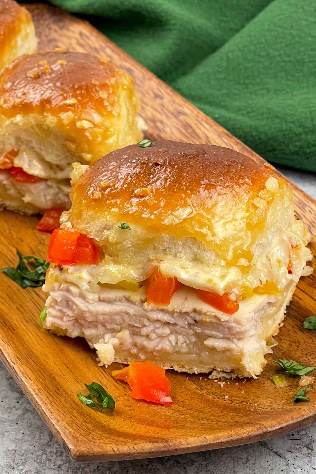 Kentucky Hot brown sliders served on a wooden tray, showing layers of sliced turkey, melted cheese, red peppers, and a creamy sauce inside glossy golden buns.