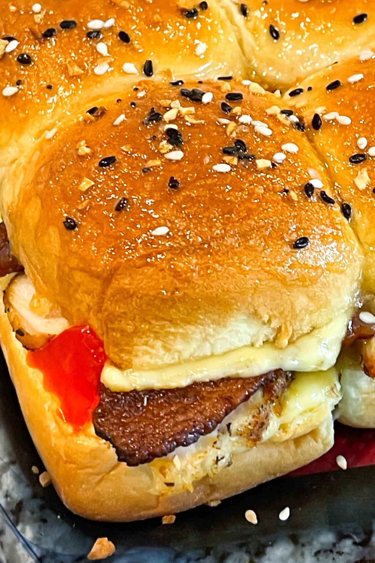 Close up of Kentucy Hot Brown Sliders in a glass baking dish showing crispy bacon, melted cheese and red peppers isnide soft, golden buns topped with everything bagel seasoning.