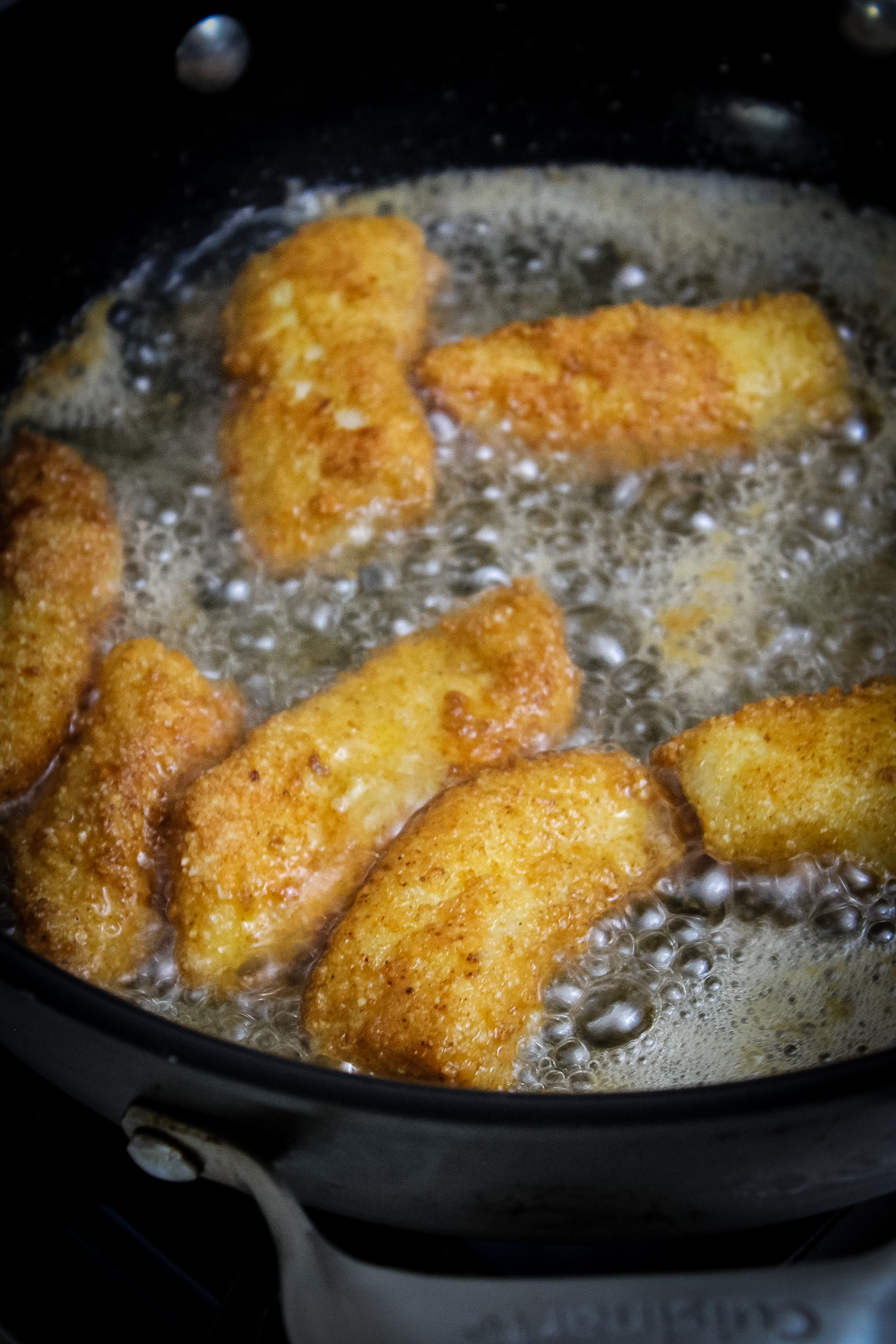 Golden grown breaded gluten Free Fish Sticks sizzling in hot oil inside a black skillet during the frying process.