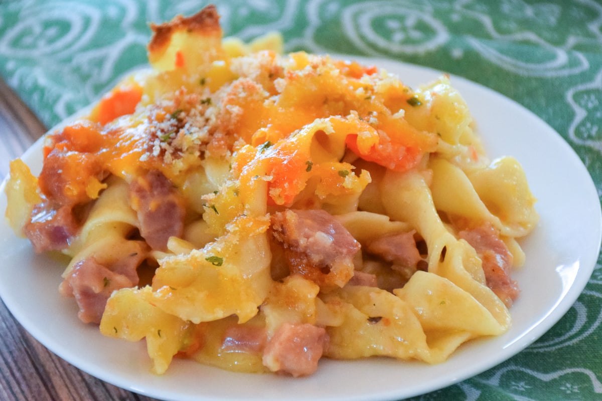 A serving of leftover ham and noodle casserole on a white plate with a green and white patterned napkin.
