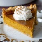 A close up of a slice of maple pumpkin pie topped with whipped cream and sprinkled with cinnamon.