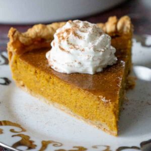 A close up of a slice of maple pumpkin pie topped with whipped cream and sprinkled with cinnamon.