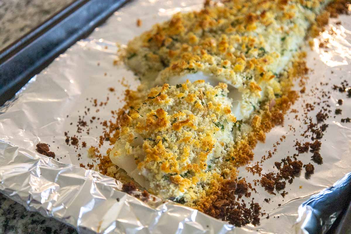 A foil lined sheet holding a large fillet of haddock covered in toasted golden breadcrumbs, fresh from the oven.