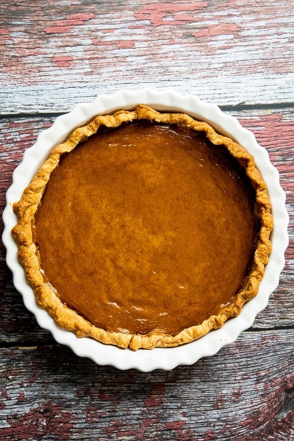 Overhead image of a whole baked pie in a white fluted ceramic pie dish on a rustic wooden surface.