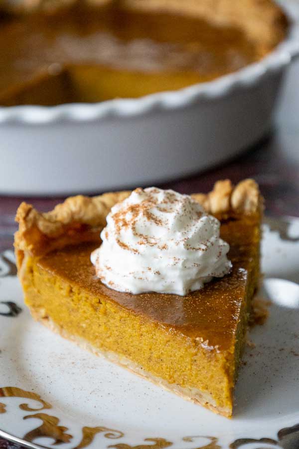 A close up of a slice of maple pumpkin pie topped with whipped cream and sprinkled with cinnamon.