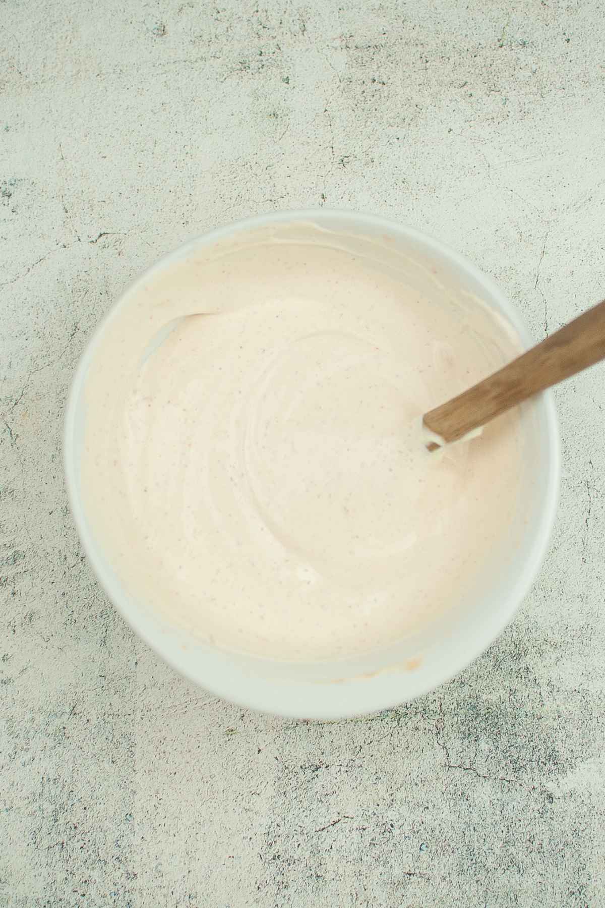 A white mixing bowl filled with freshly blended sauce with a wooden spoon handle resting inside.