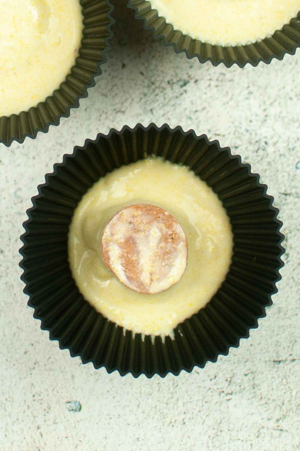 Close up of muffin liner filled with cornbread batter and a round slice of sausage placed in the center, ready to be cooked.