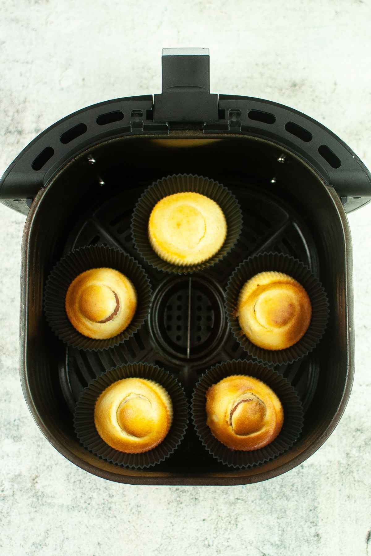 Six golden brown sausage corn dog muffins in black silicone liners arranged inside an air fryer basket, freshly cooked and lightly browned on top.