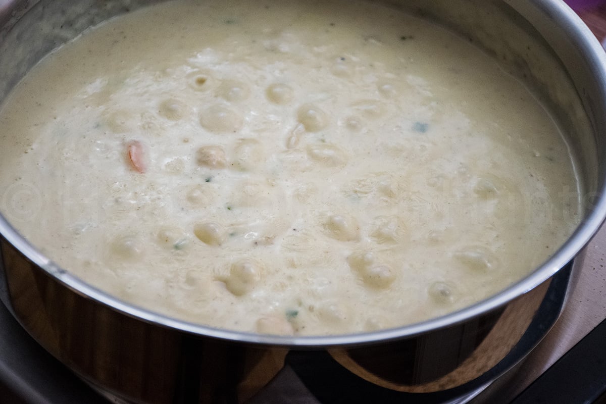 A close up of a creamy seafood sauce simmering in a stainless steel pot, with visible shrimp and bubbling on the surface.
