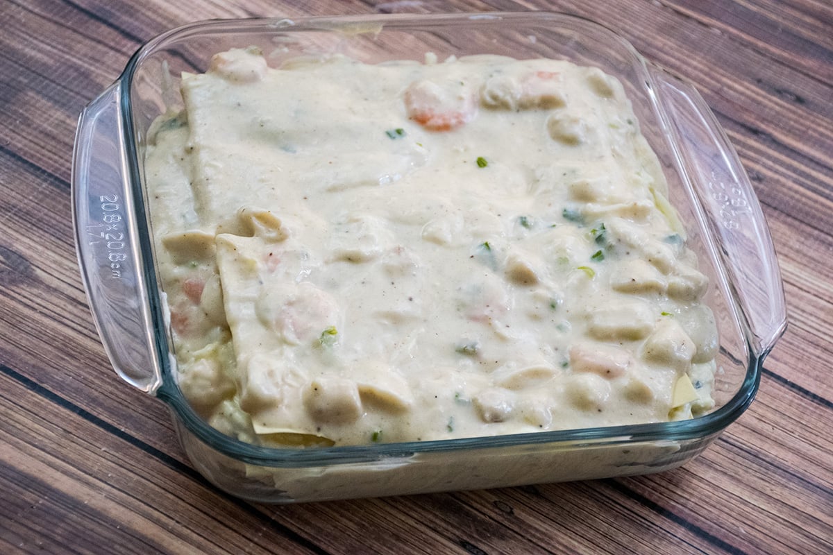 A glass baking dish filled with unbaked lasagna with a creamy white sauce.