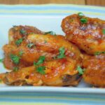 Close up of sweet chili chipotle wings on a white rectangular plate, garnished with chopped fresh cilantro. The wings are coated in a glossy, reddish orange sauce with visible seasoning.