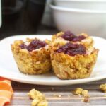 Close up of three Thanksgiving stuffing muffins on a white plate, sowing crispy edges and a center of mashed potatoes and cranberry sauce.