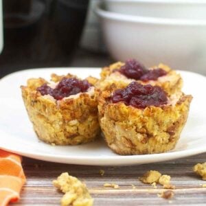 Close up of three Thanksgiving stuffing muffins on a white plate, sowing crispy edges and a center of mashed potatoes and cranberry sauce.