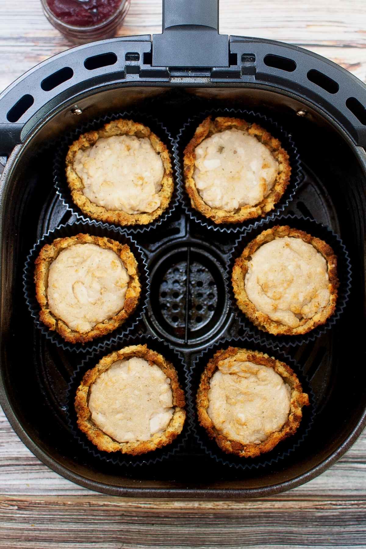 Six stuffing muffin cups in a black air fryer basket, each filled with mashed turkey and lightly browned from cooking.