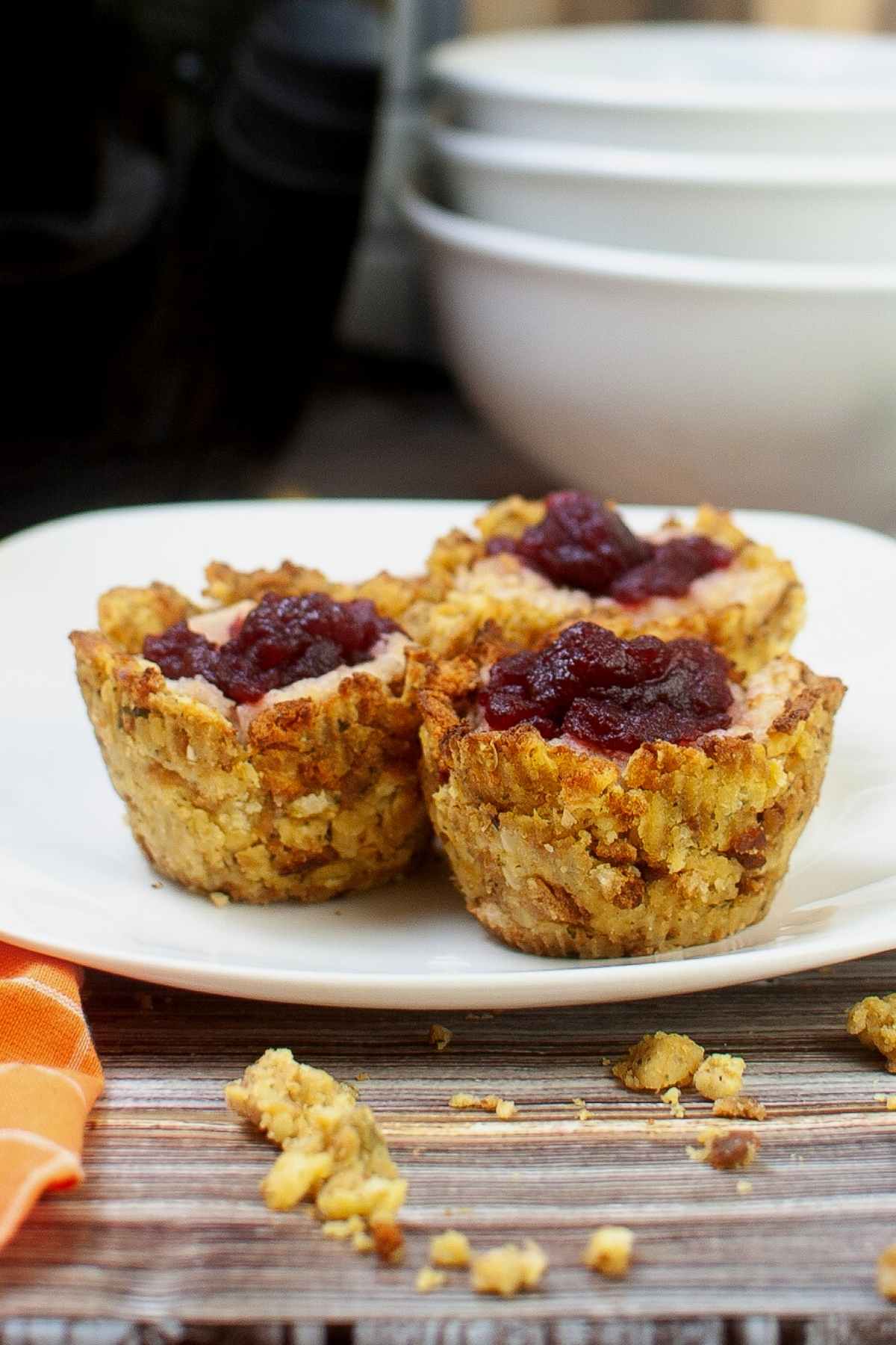 Close up of three Thanksgiving stuffing muffins on a white plate, sowing crispy edges and a center of mashed potatoes and cranberry sauce.