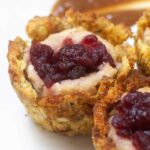 Extreme up close of a stuffing muffin topped with mashed potatoes and chunky cranberry sauce, highlighting the crispy edges.