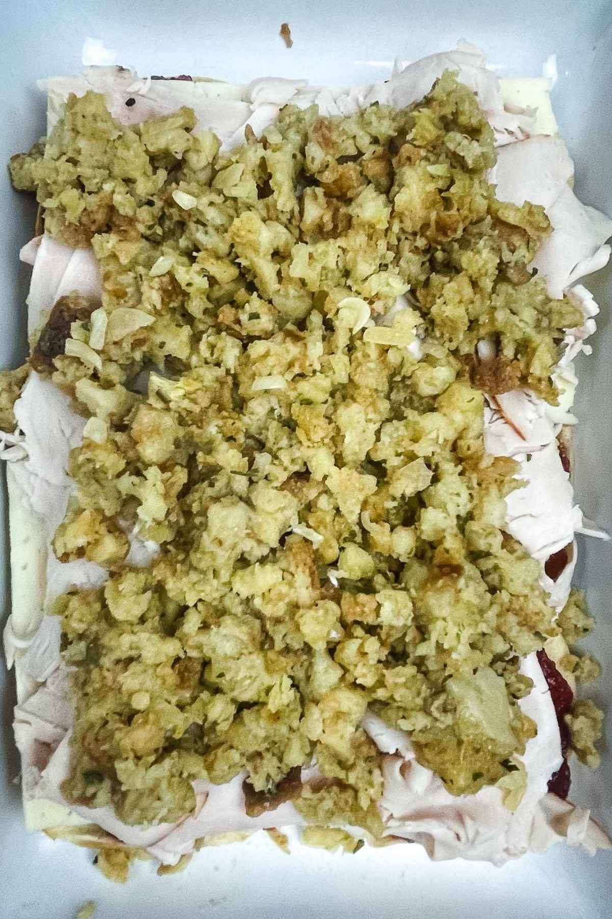 A layer of stuffing spread over turkey slices in a baking dish, showin the filing for the slider recipe.