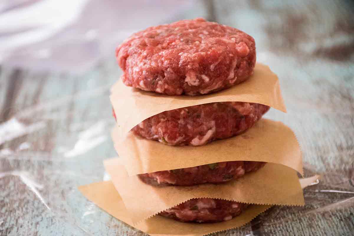 Stack of raw venison breakfast sausage patties separated by squares of parchment paper, ready for storage or cooking.