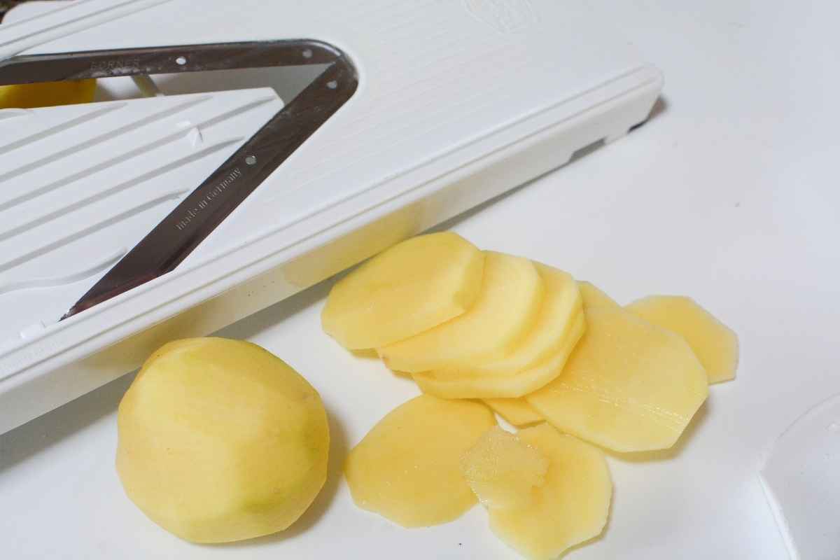 Peeled yellow potatoes sliced thinly with a mandoline slicer on a white cutting surface.