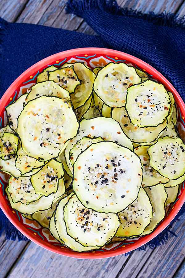 Close up of a red bowl filled with crispy zucchini chips sprinkled with everything bagel seasoning.