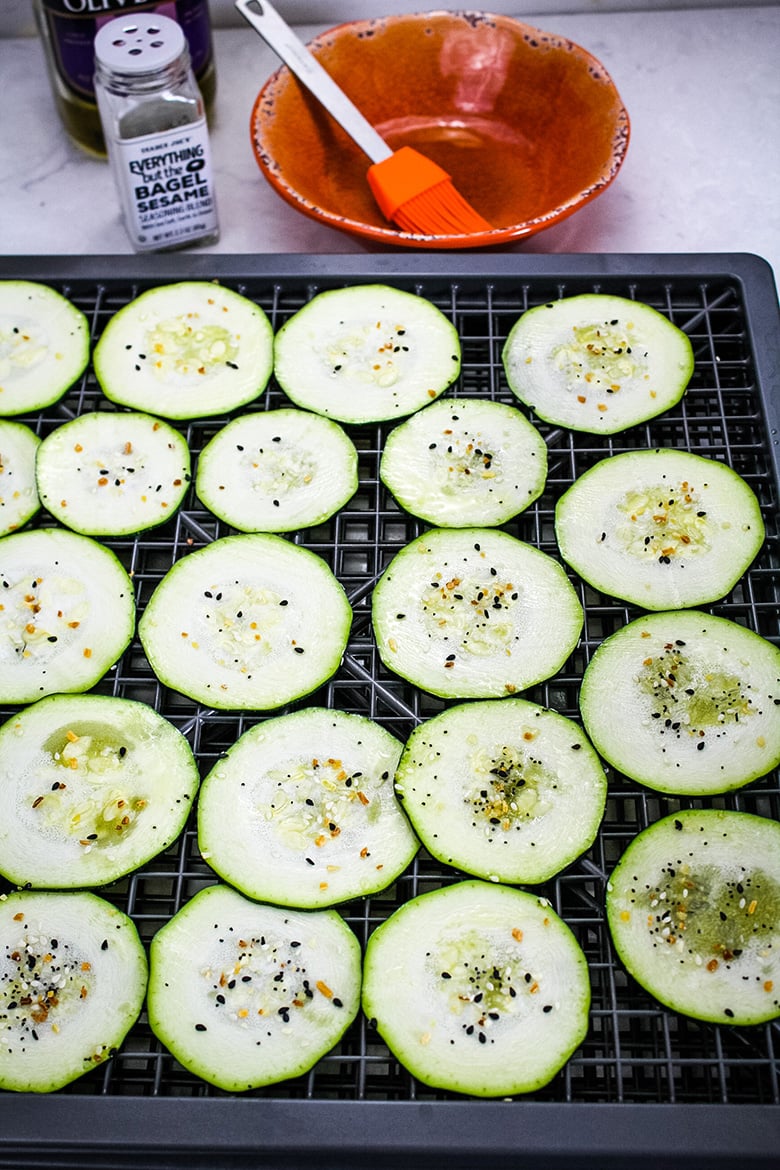 Raw zucchini slices arranged on a dehydrator tray, topped with everything bagel seasoning.