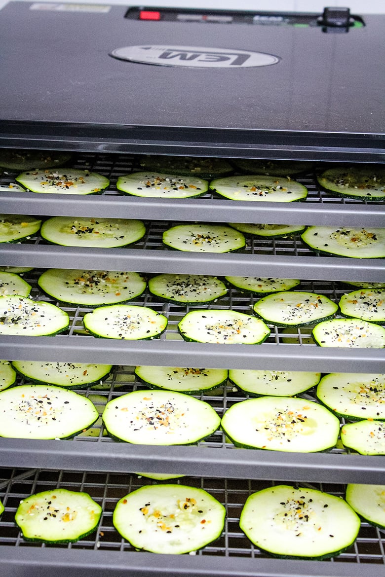 Multiple trays inside a dehydrator filled with zucchini slices sprinkled with everything bagel seasoning.